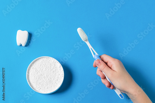 A child holds a toothbrush with silicone bristles against the background of tooth powder and a tooth figurine.