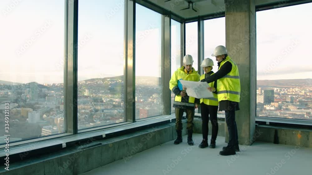 Group of engineers with blueprints standing on construction site, talking.