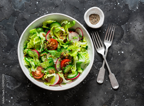Easy vegetarian vegetable salad with fresh vegetables. Cherry tomatoes , romano lettuce, cucumbers, radishes and french mustard, olive oil, lemon salad dressing on a dark background, top view. 