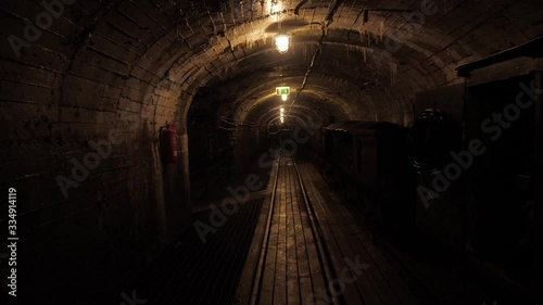 poorly lit wet damp mine tunnel with rails on the floor and a train trolley