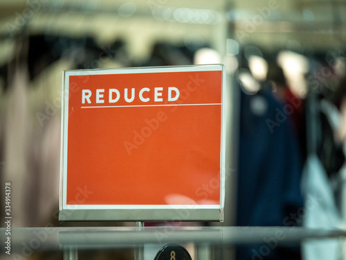 Orange reduced price sale sign on clothing rack in department store