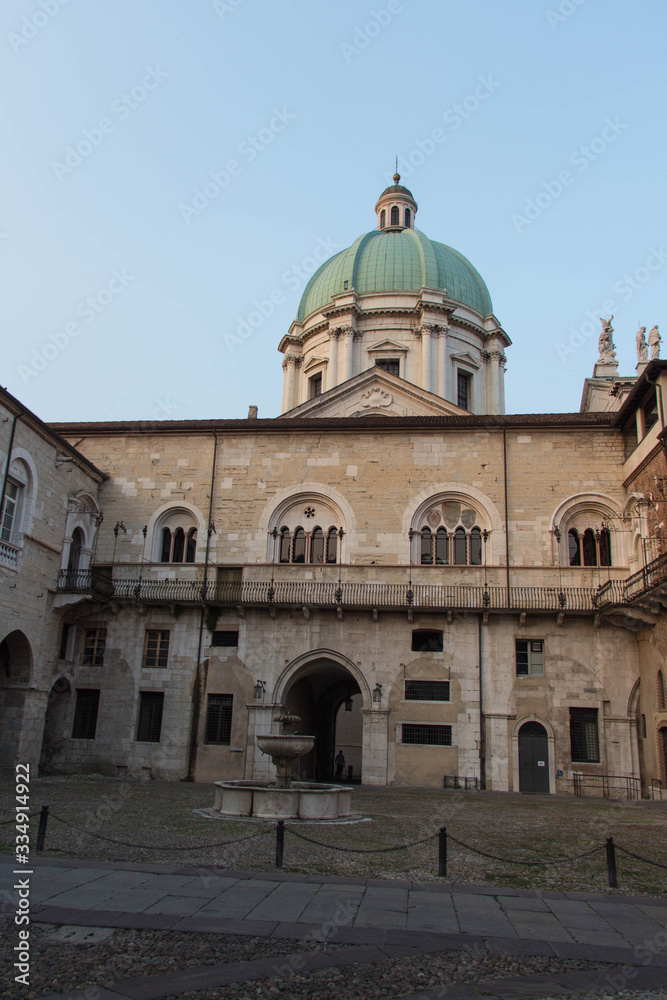 Fountain in the inner yard of medieval palace Palazzo del Broletto with dome of the New Cathedral on background, Brescia, Lombardy, Italy.