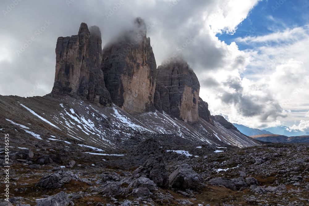 Italian Dolomites, Tre Cime - View of Tre Cime, three peaks of the small, grande, east mountains, which are partially shrouded in clouds. There are snow on the walls of the mountains.