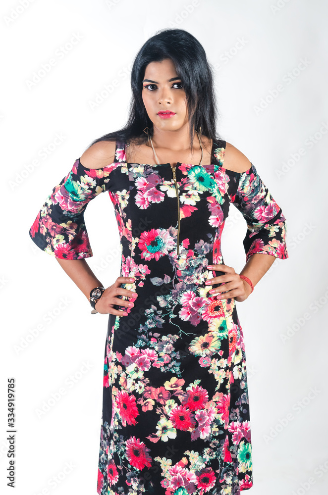 Young woman in a floral pattern dress standing with her hands on her looking away slightly to the right
