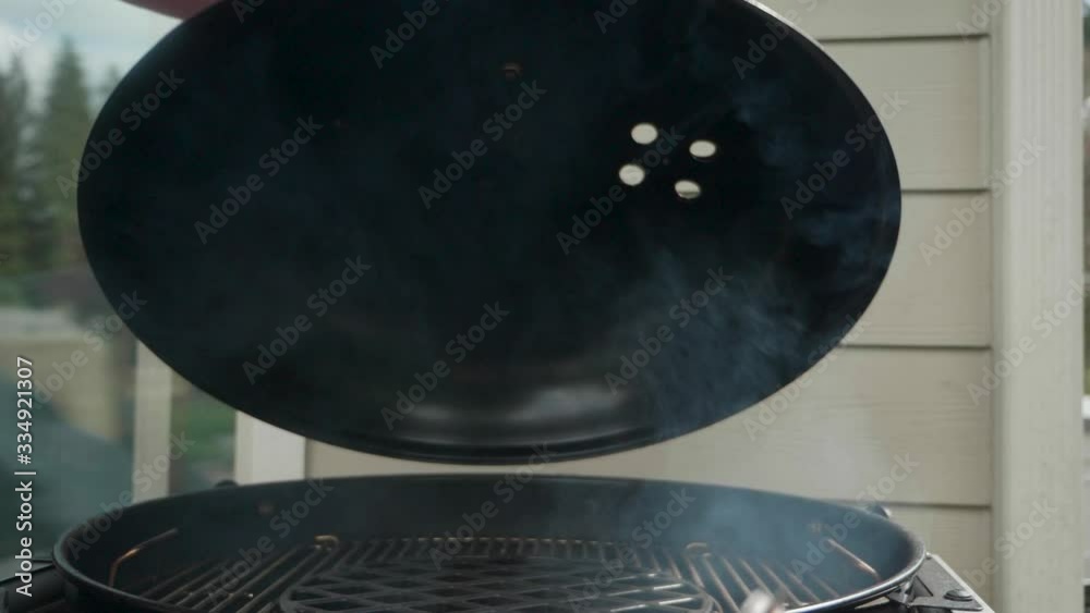 Lifting lid off a hot charcoal grill and checking the temperature in