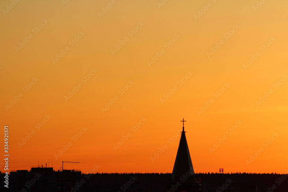Sun below the horizon and the roof of the church with a cross on the background fiery dramatic orange sky at sunset or dawn backlit by the sun. Place for text and design.
