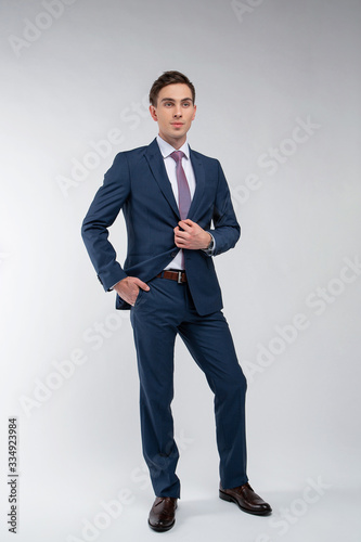 Young, handsome man in a blue suit in a white shirt with a tie on a white background in studio