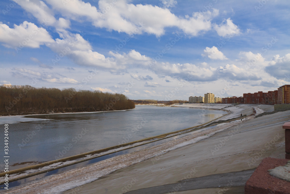 The deserted embankment of the white river in April, the Bank in the snow, the naked forest against the blue sky on a Sunny day in the city