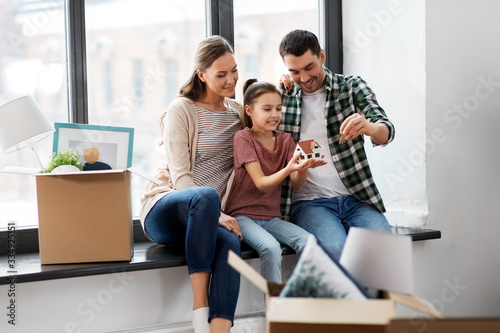 mortgage, family and real estate concept - happy mother, father and little daughter with house model and stuff in boxes moving to new home