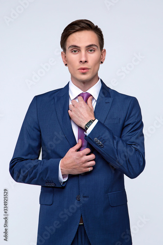 Young, handsome man in a blue suit in a white shirt with a tie on a white background in studio