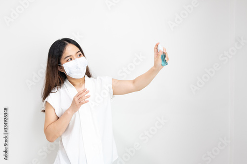 Close up of Asian girl wearing protective mask using alcohol antiseptic gel with copy space, isolated on white background. Concept of Coronavirus COVID-19, Coronavirus disease pandemic.