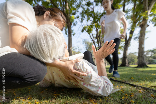 Exhausted asian senior woman lying on the ground after falling down from the sunburn,heat stroke,sunny day in summer hot weather,daughter care help support her elderly mother with faint,dizzy,syncope
