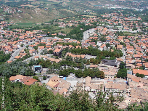 View from above of the tiled roofs of ancient houses of a small state under the rays of the summer sun surrounded by garden trees.