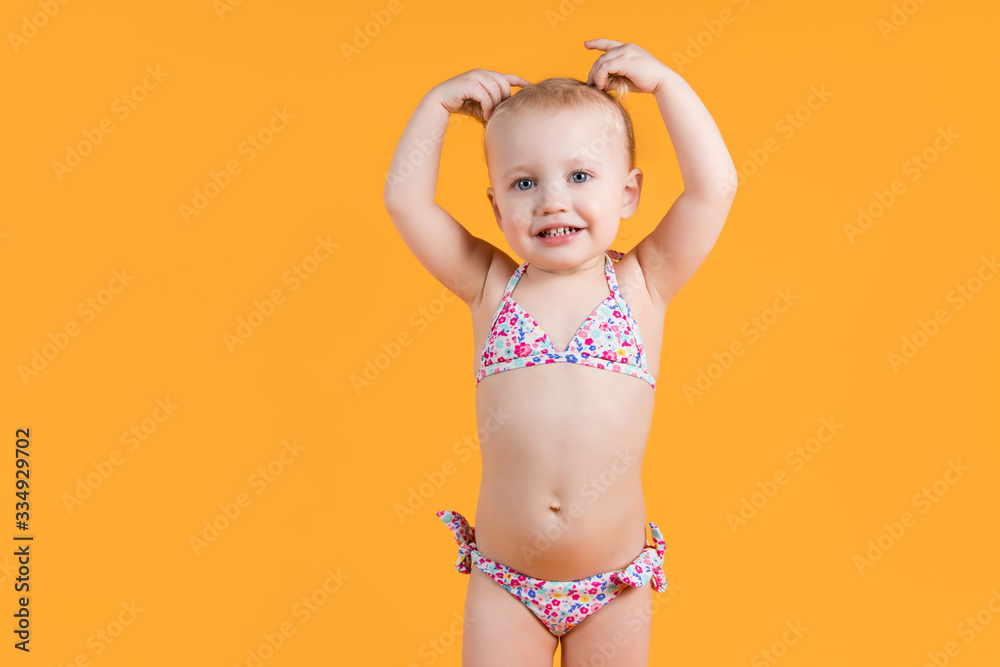 little girl in a swimsuit smiles and holds hands with ponytails on her head little girl in a swimsuit smiles and holds hands with ponytails on her head