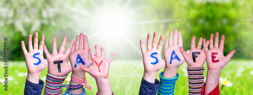 Kids Hands Holding Colorful English Word Stay Safe. Sunny Green Grass Meadow As Background