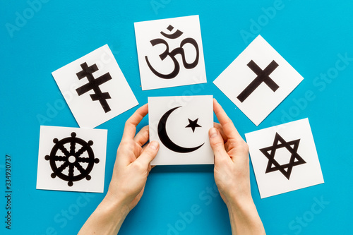 Choose religion concept. Hand with Islam crecent near world religions symbols on blue background top view photo