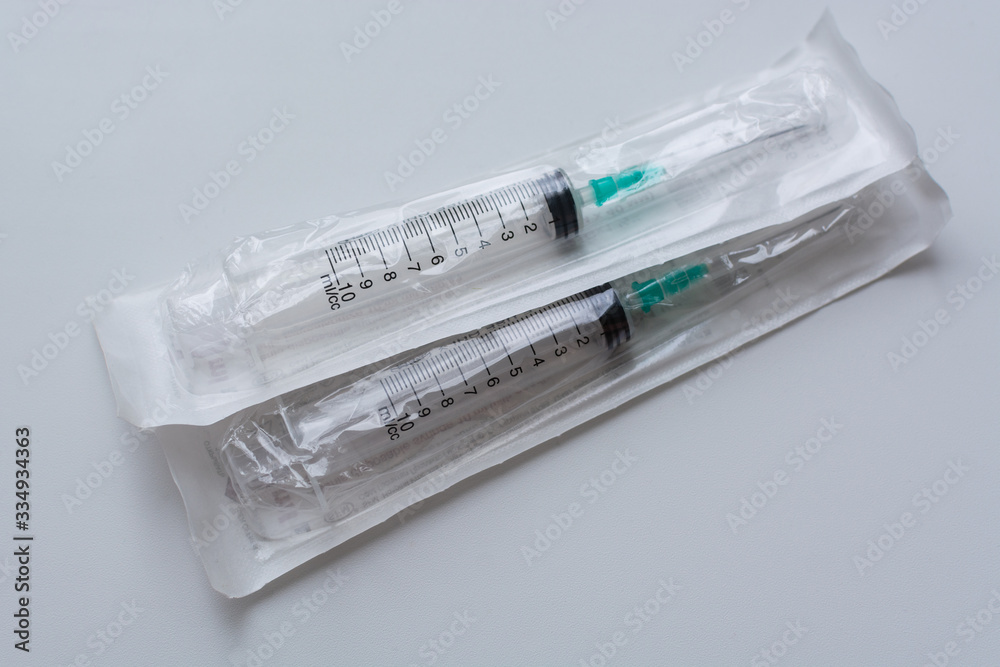 Disposable medical syringes in a package lie on top of each other on a uniform light gray background Disposable medical syringes in a package lie on top of each other on a uniform light gray background