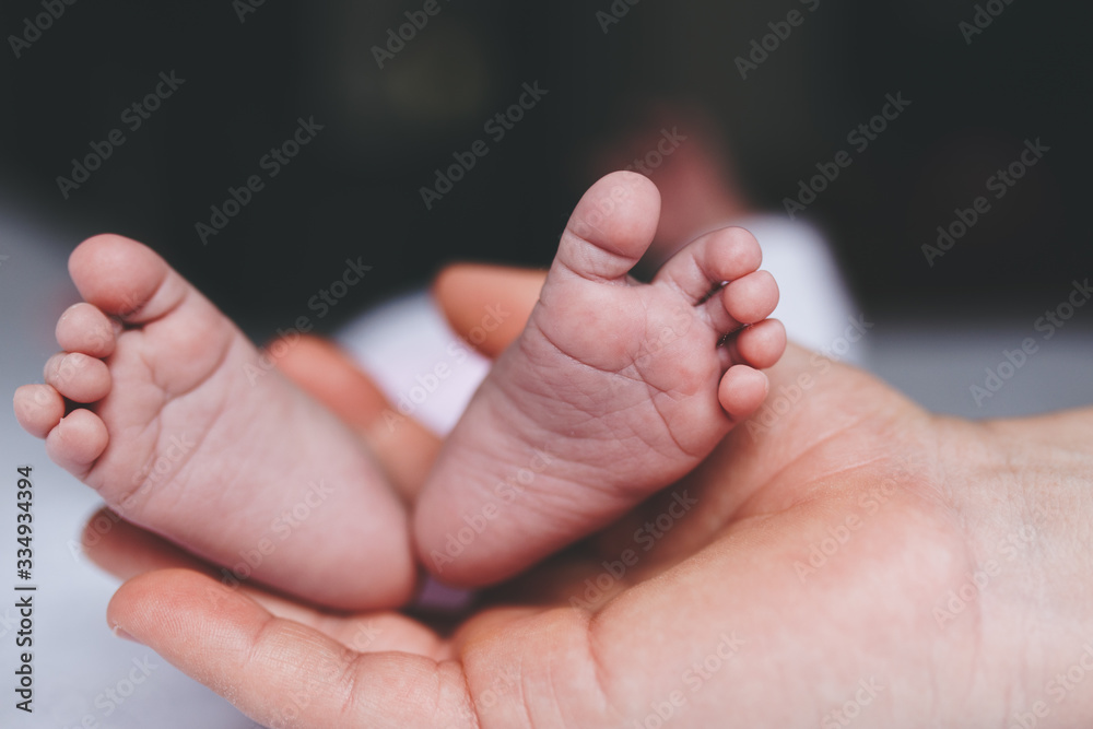 close up of a mother's hand holding her baby's feet close up of a mother's hand holding her baby's feet