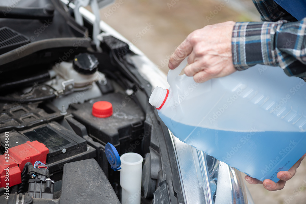 Fototapeta premium Hands of mechanic pouring windshield washer fluid in a car