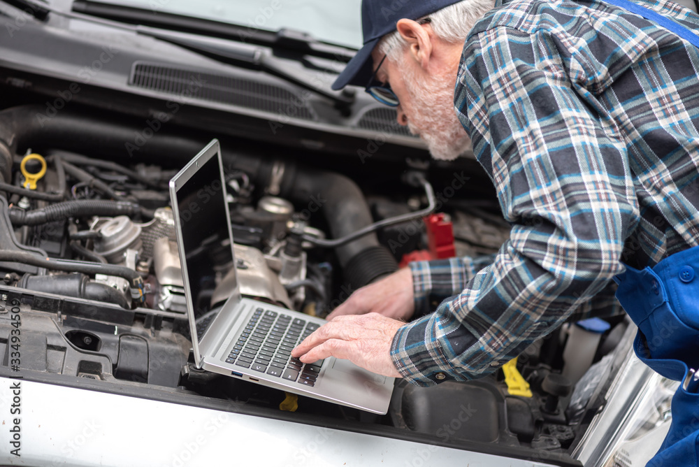 Mechanic using laptop for checking car engine Mechanic using laptop for checking car engine