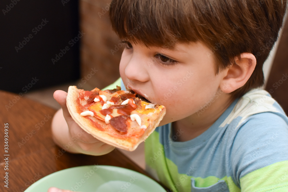 Happy boy eats pizza. Child eating pizza, ordering fast food for dinner
