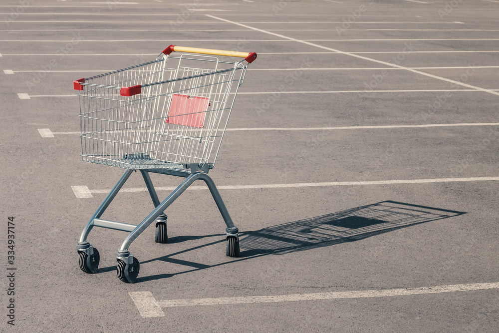 Empty grocery cart in an empty parking lot near a supermarket. Financial crisis, quarantine, lack of money concept Empty grocery cart in an empty parking lot near a supermarket. Financial crisis, quarantine, lack of money concept