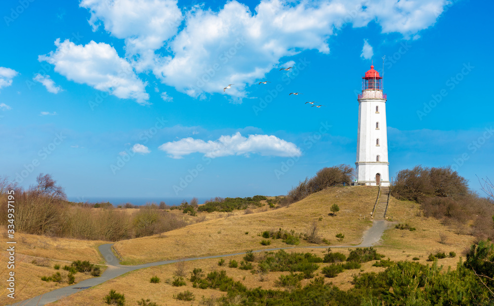 The Dornbusch lighthouse on the German island of Hiddensee in the Baltic Sea. It is a beautiful winter day with blue sky and clouds. A flock of seagulls flies in the sky.