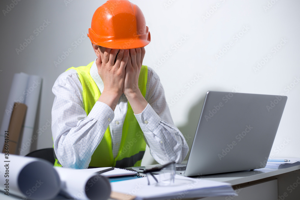 Crisis concept. An unemployed man is sad while sitting at his workplace. Depressive state, stress at the engineer in a helmet. Crisis concept. An unemployed man is sad while sitting at his workplace. Depressive state, stress at the engineer in a helmet.