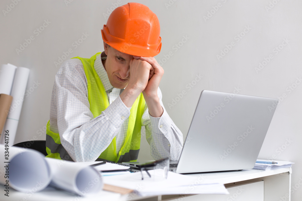 Crisis concept. An unemployed man is sad while sitting at his workplace. Depressive state, stress at the engineer in a helmet.