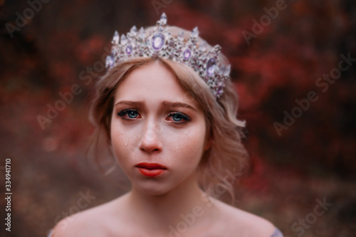 Portrait сlose-up young beauty face woman. Princess upset cry sad. sadness tears in blue beautiful eyes. Blonde hair elegant hairstyle silver vintage luxury diadem crown. backdrop autumn nature forest