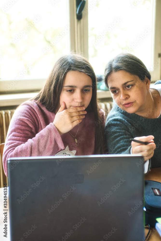 Fototapeta premium little girl carries out homework at home on the laptop helped by her mother