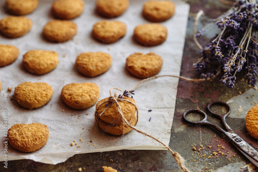 Freshly baked heart-shaped cookies on parchment paper, lavender flower Freshly baked heart-shaped cookies on parchment paper, lavender flower