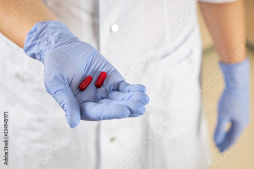 Nurse holds two red pills in her palm as a cure for the virus