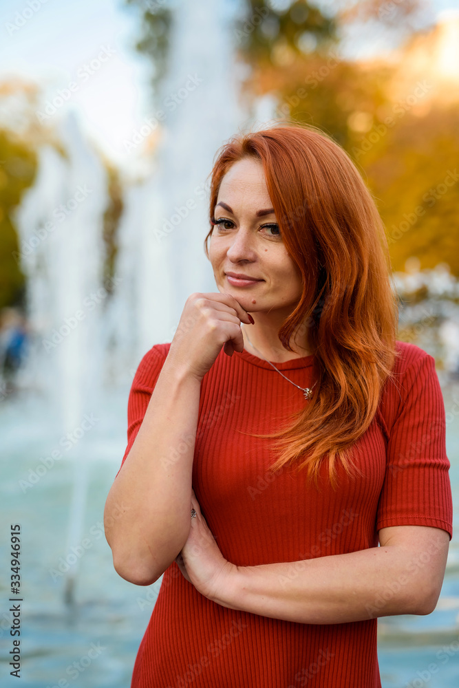 Portrait of young woman in casual wear posing near fountain outdoors. Autumn in city