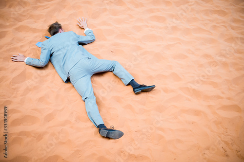 Unconscious businessman lying face down down collapsed on red sand desert background
