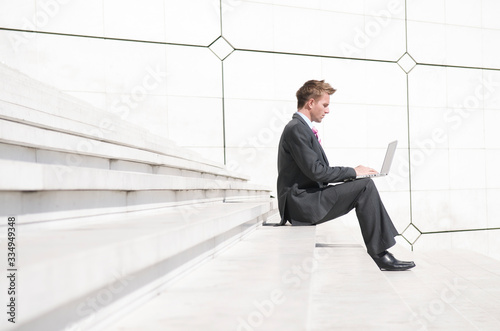 Businessman sitting outdoors on minimalist marble steps using his laptop computer 