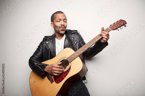 African bearded man playing guitar wearing leather black jacket isolated on white background.