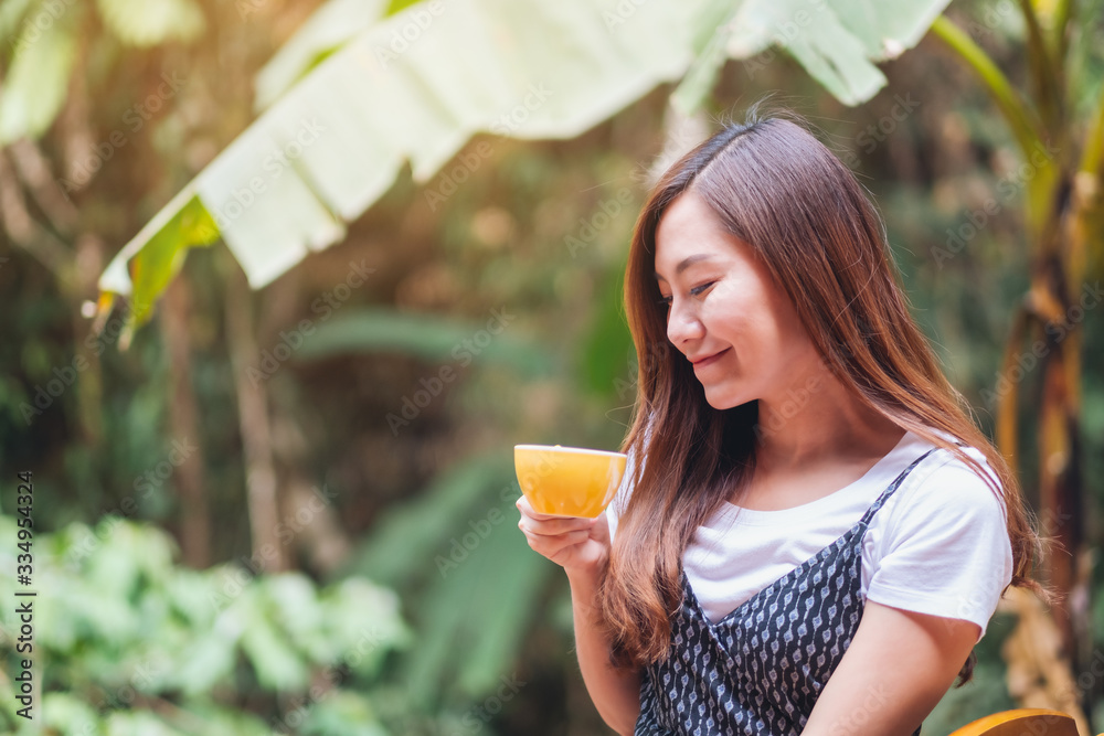 Fototapeta premium Closeup image of a beautiful asian woman holding and drinking hot coffee in the outdoors