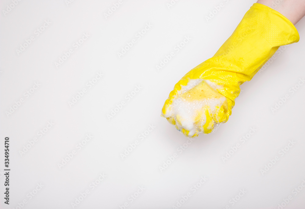 Hand in an yellow rubber glove with an yellow sponge and foam on a white background. Washing dishes, cleaning, home cleaning. Hand in an yellow rubber glove with an yellow sponge and foam on a white background. Washing dishes, cleaning, home cleaning.