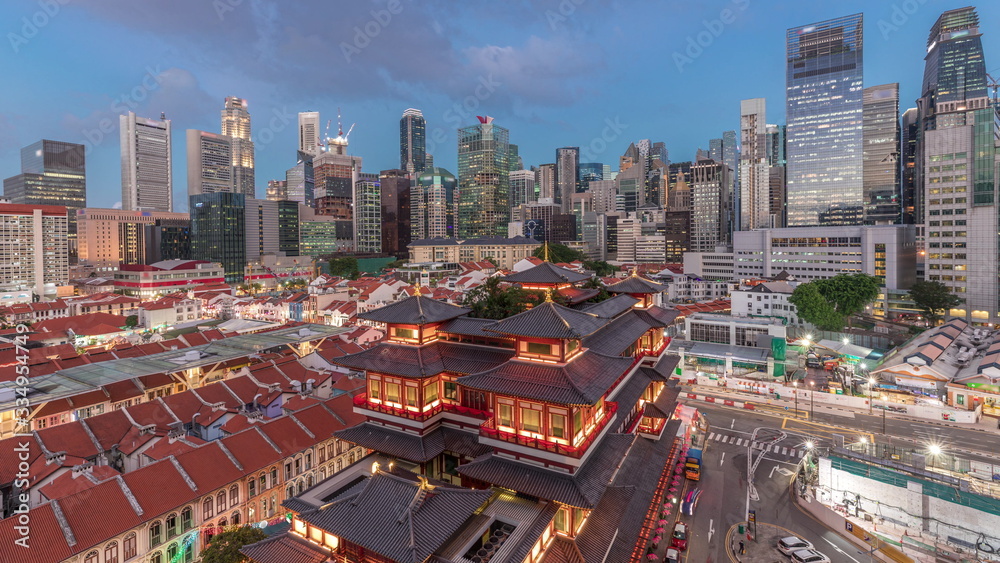 Obraz premium The Buddha Tooth Relic Temple comes alive at night in Singapore Chinatown day to night timelapse, with the city skyline in the background.