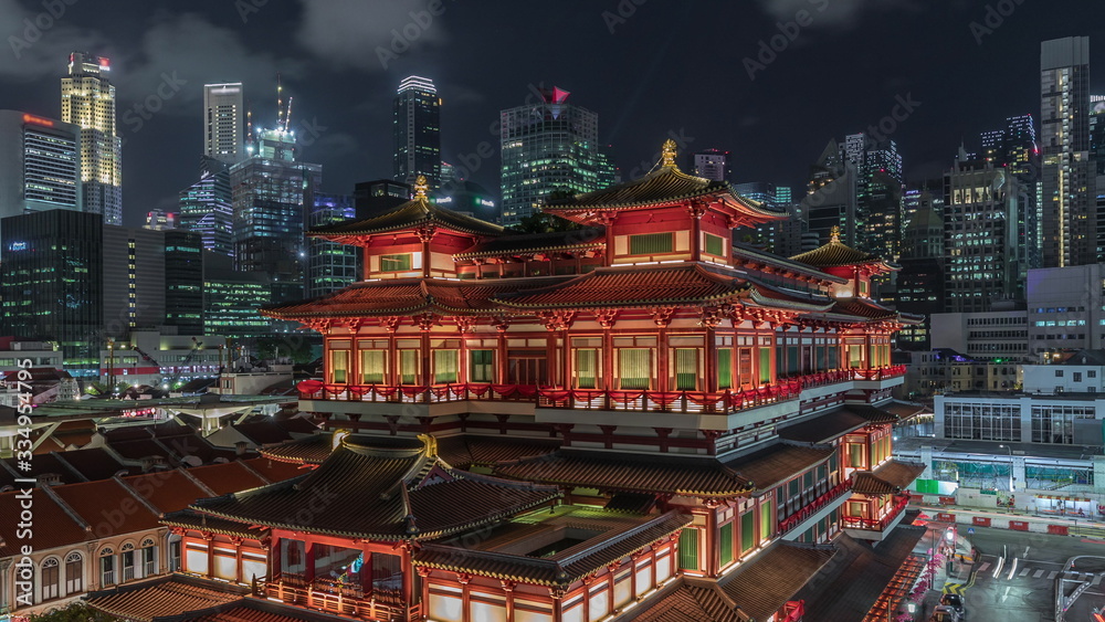 Obraz premium The Buddha Tooth Relic Temple comes alive at night timelapse in Singapore Chinatown, with the city skyline in the background.