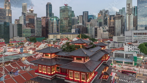 The Buddha Tooth Relic Temple comes alive at night in Singapore Chinatown day to night timelapse, with the city skyline in the background. © neiezhmakov