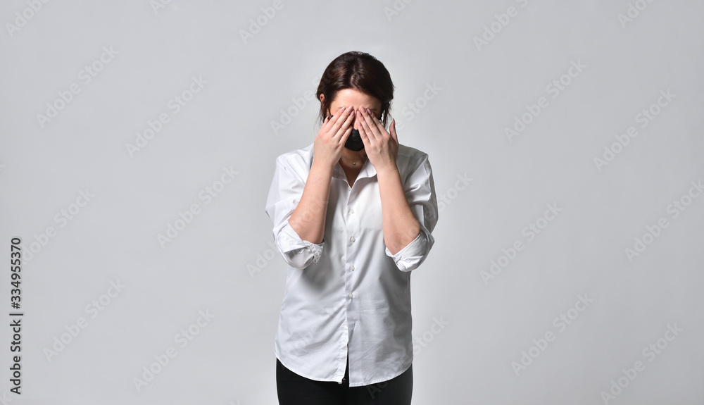 A tired woman in a black protective mask covers her face with her hands against a white background, during the coronavirus pandemic. The concept of viral danger, stress and fear. A tired woman in a black protective mask covers her face with her hands against a white background, during the coronavirus pandemic. The concept of viral danger, stress and fear.