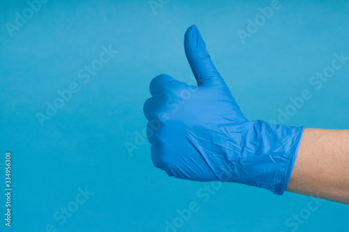 Blue Glove and thumb up with blue background. Close up. Copy space