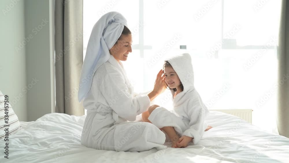 Young cute mother and daughter dressed in dressing gowns after a shower hugging on a large bed. Young cute mother and daughter dressed in dressing gowns after a shower hugging on a large bed.