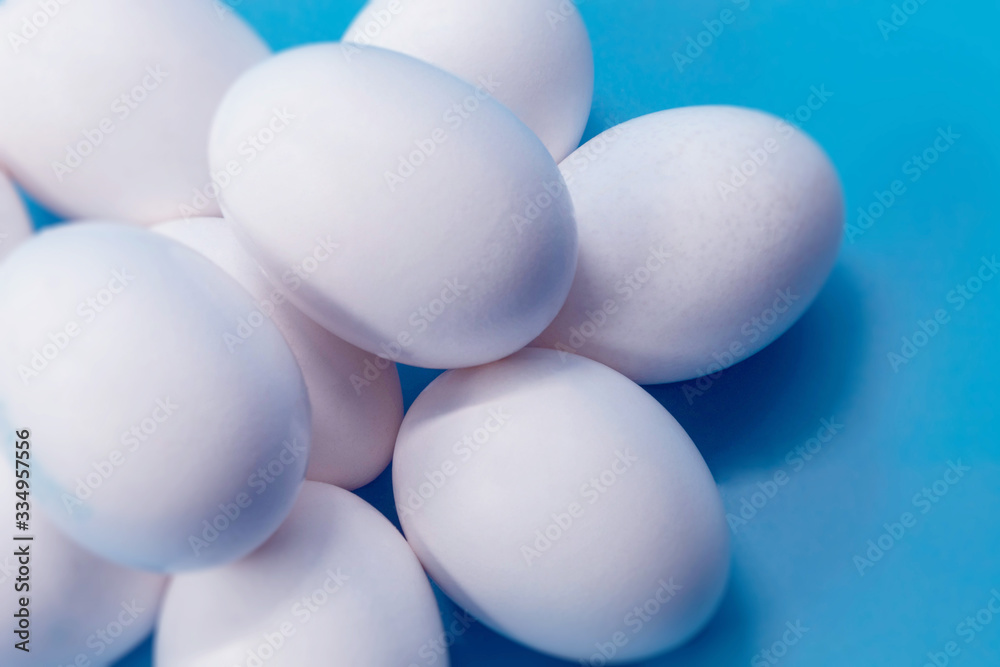 Whole white chicken eggs are lying on a blue background, close-up