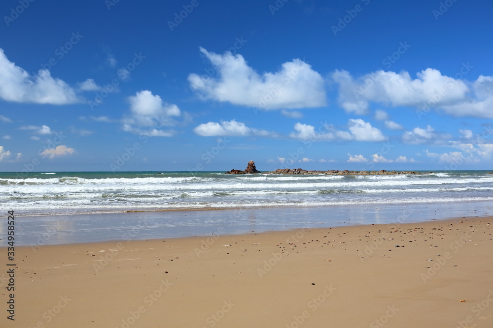 Seascape. Blue sky with white clouds. Surf. Golden sand.