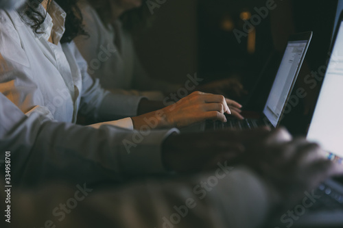 Cropped shot of business people working with laptops. Close-up partial view of professional business colleagues using laptop computers in dark office. Technology concept