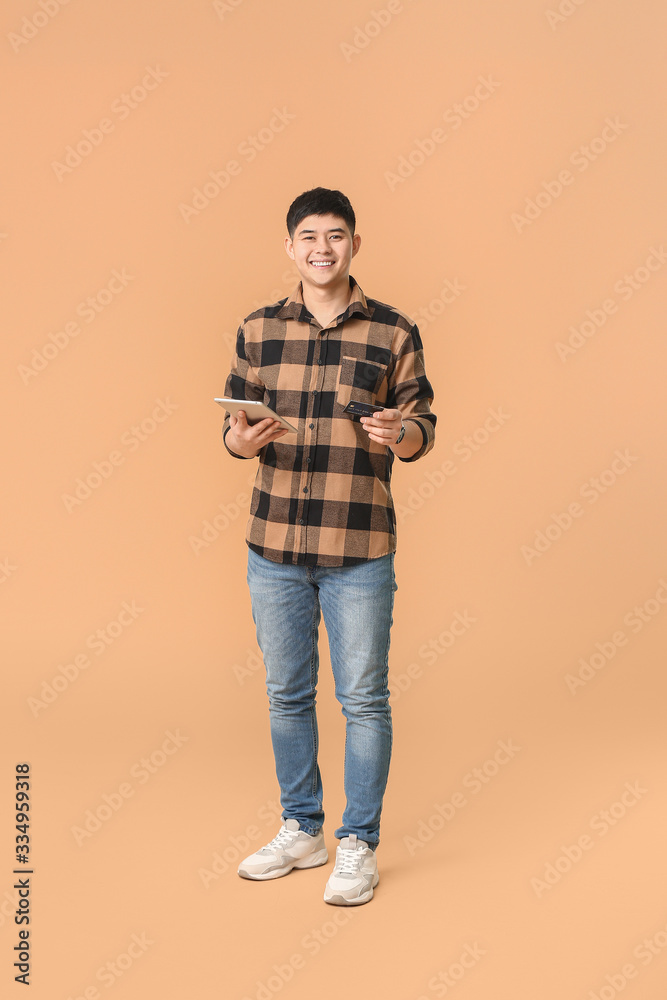 Fototapeta premium Asian man with credit card and tablet computer on color background