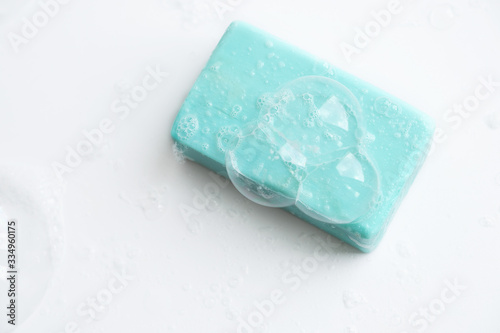A piece of blue soap in soap bubbles on a white background, top view.